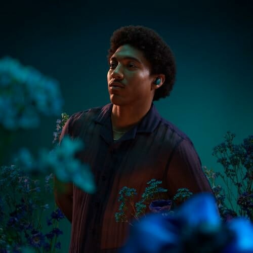A person wearing earbuds standing among blue flowers against a dark background