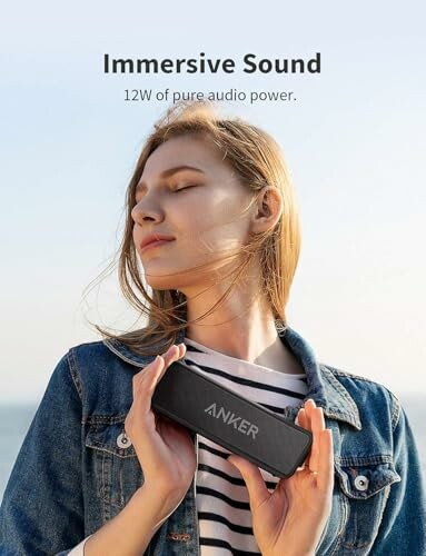 Woman holding Anker speaker outdoors with text 'Immersive Sound 12W of pure audio power'.